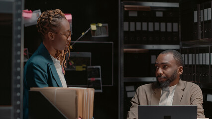 Two investigators studying forensic evidence on wall map, discussing criminal information in...