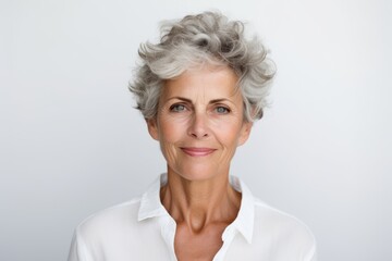 Portrait of smiling senior woman with grey hair against grey background.