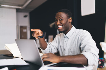 Cheerful black man smiling and pointing during work