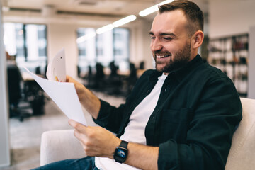 Positive male entrepreneur reading documents and laughing