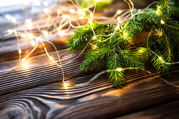 Border with green spruce branches with Christmas lights on a wooden background. Pine tree, Christmas evergreens.