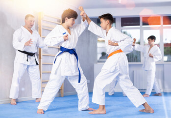Concentrated teen boys in kimonos honing punching techniques during kumite at karate training session under guidance of sensei..