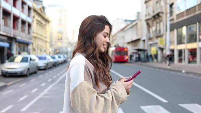 Happy young woman is using her mobile phone and enjoying the city