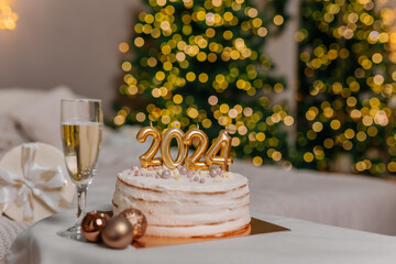 a cake with 2024 candles in Christmas decorations. A glass of champagne. Preparations for family dinner, home recipes, cooking chocolate cake. beige golden background