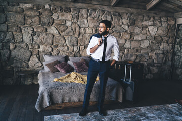 Bearded businessman passing time standing in bedroom of hotel