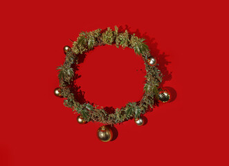 Cannabis leaves and buds in the shape of a Christmas wreath on a red background. Holiday creative concept - 673523874