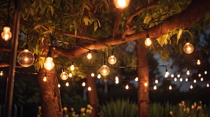 Tuinposter Decorative outdoor string lights hanging on tree in the garden at night time © Ziyan