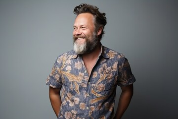 Portrait of a handsome man with long gray beard and mustache, wearing a shirt, looking at the camera and smiling while standing against grey background