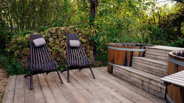 Wooden chairs stand near large vats of hot and cold water for relaxation in country complex in the forest