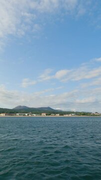 Coroso Beach in Santa Ux&iacute;a de Ribeira. Slow-motion of the azure sea, revealing the coastline with houses and distant lush mountains under a summer sky adorned with wispy clouds.