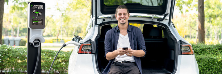 Man using smartphone online banking application to pay for electric car battery charging from EV...