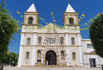 The Mision de San Jose Church in San Jose del Cabo, Mexico. The building is decorated with strings of green and yellow triangular flags against a blue sky.