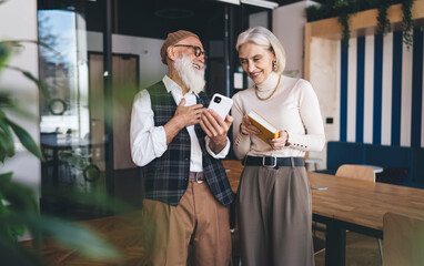 Smiling senior coworkers reading news on smartphone in office