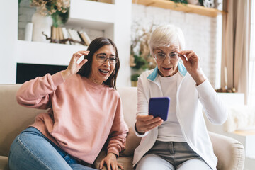 Senior diverse girlfriends smiling while browsing cellphone