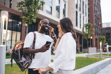 Cheerful multiethnic friends sharing earphones on street