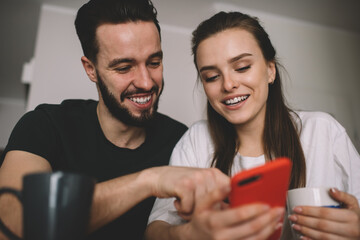 Laughing young couple viewing photos on smartphone together in cafe