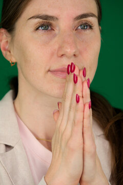 on a green background, chromakey, close-up of a woman with emotions in a beige jacket, red manicure, blue eyes This is an image of young business woman praying. High quality photo