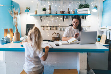 Cheerful woman and daughter working and studying at kitchen counter