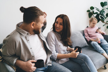 Happy couple sitting on sofa talking while daughter using smartphone