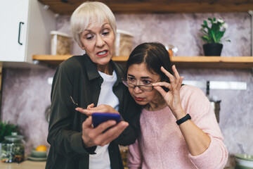 Diverse women standing with smartphone in kitchen at home