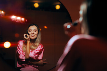 Woman Using Highlighter on Her Cheekbones Looking in the Mirror. Girl using cosmetic product to enhance her glow 
