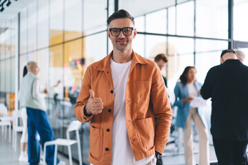 Half length portrait of Caucasian male entrepreneur showing OK and looking at camera during working day in office enterprise, successful employee in optical eyewear for vision protection posing