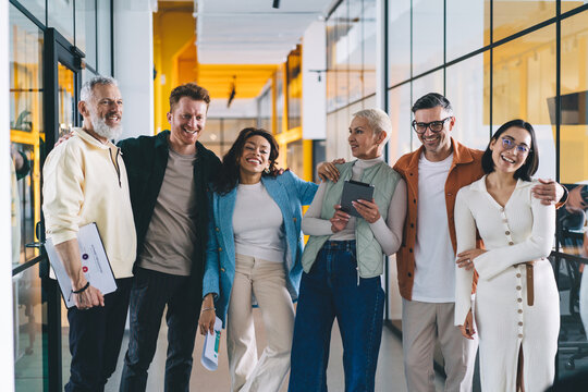 Group of cheerful multiracial colleagues standing near office glass wall