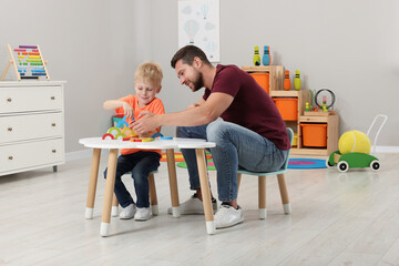 Motor skills development. Happy father helping his son to play with colorful wooden arcs at white table in room