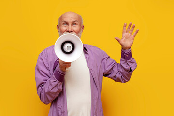 old bald grandfather announces information through megaphone on yellow isolated background,...