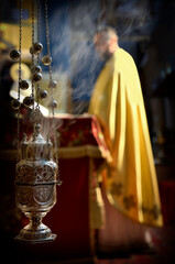 Old silver triple chain censer with burning charcoal inside, cloud of smoke, priest in background...