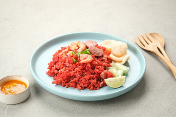 Nasi Goreng Merah, traditional food from Makassar, Indonesia. Fried rice with tomato sauce, shrimp, meatballs and egg. Served with pickled cucumber, chili sauce and lime
