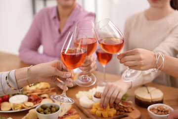 People clinking glasses with rose wine above table indoors, closeup