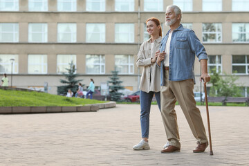 Fototapeta na wymiar Senior man with walking cane and young woman outdoors. Space for text