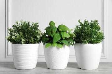 Different artificial potted herbs on wooden table near white wall