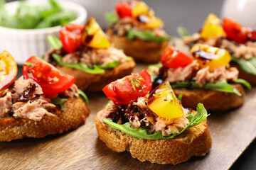 Delicious bruschettas with balsamic vinegar, tomatoes, arugula and tuna on wooden table, closeup