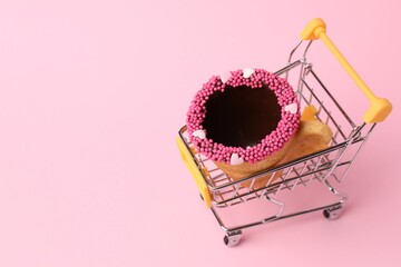 Delicious edible biscuit coffee cup decorated with sprinkles in shopping cart on pink background,...