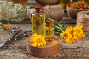 Bottles of essential oils, calendula flower and scissors on wooden table. Medicinal herbs