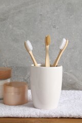 Bamboo toothbrushes in holder, towel and cosmetic products on wooden table