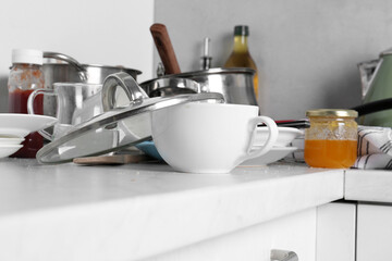 Many dirty utensils and dishware on countertop in messy kitchen, closeup