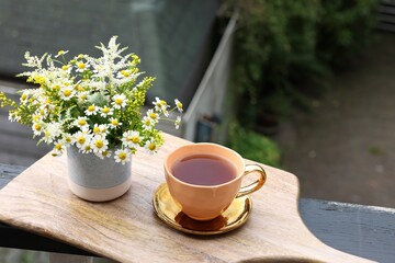 Cup of delicious chamomile tea and fresh flowers outdoors. Space for text