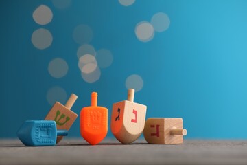 Different dreidels on wooden table against light blue background with blurred lights, space for...