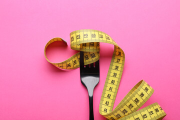 Fork with measuring tape on pink background, top view. Diet concept