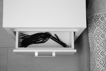 Black leather whip in open drawer of bedside table indoors, above view. Sex toy - obrazy, fototapety, plakaty