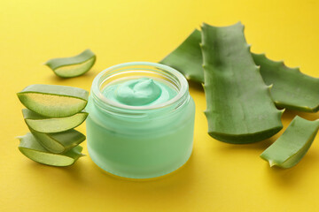Jar with cream and cut aloe leaves on yellow background, closeup