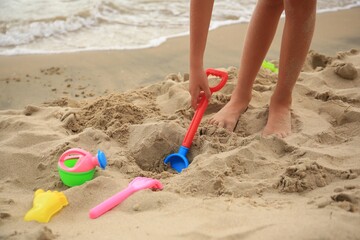 Little girl playing with plastic toys on sandy beach, closeup