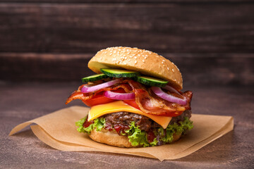 Tasty burger with bacon, vegetables and patty on textured table