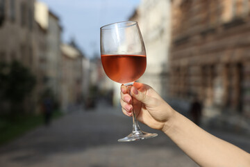 Woman holding glass of rose wine outdoors, closeup