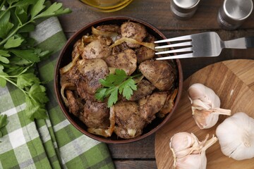 Tasty fried chicken liver with onion and parsley served on wooden table, flat lay