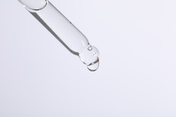 Dripping cosmetic serum from pipette on white background, space for text