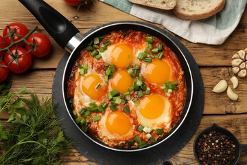 Delicious Shakshuka in frying pan served on wooden table, flat lay
